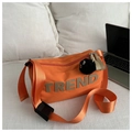 Close-up of orange canvas bag with TREND lettering and black plush charm on white bedding - With Pendant / Orange