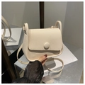 Detail of cream lychee texture saddle bag featuring a round magnetic clasp and thin strap - Off White