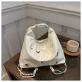 Elegante bolso beige con remaches de mariposa plateados y cadena sobre mesa de cristal - Blanco