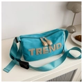 Macro shot of blue nylon crossbody bag with TREND letter patch on a white table - Blue