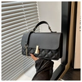 Detalle de costuras acolchadas y hebilla dorada en un bolso de cuero negro sostenido - Negro