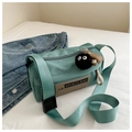 Close-up of green cylinder bag with vintage sports label and plush charcoal charm - With Pendant / Green