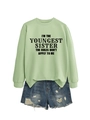 Detail of sage green sweatshirt with black slogan print paired with ripped denim shorts - Olive Green (Black Font)