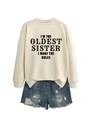 Flat lay of cream 'I'M THE OLDEST SISTER' sweatshirt paired with ripped denim shorts - Sand (Black Font)
