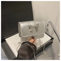 Detailed shot of a mini silver chain bag featuring a metallic bow held by hand - Silver