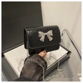 Detail of glossy black patent crossbody bag with a silver metal bow buckle and chain strap - Black