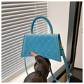 Detail of light blue quilted crossbody bag with woven handle and gold hardware in sunlight - Blue
