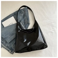 Dettaglio della borsa hobo nera lucida con ampia tracolla su sfondo di denim blu - Nero