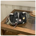 Detalle de un bolso tipo cubo negro con parches de corazones y correa de cadena plateada - Negro