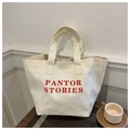 Primer plano del bolso tote de lona crema con texto Pantor Stories rojo sobre mesa madera - Blanco