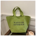 Primer plano del bolso tote de lona verde con texto PANTOR STORIES en mesa de madera - Verde