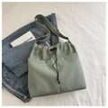 Dettaglio borsa a secchiello verde chiaro con coulisse e tasche su sfondo di tessuto - Verde