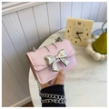Mini sac bandoulière rose avec grand nœud argenté et chaîne, porté devant un décor - Rose