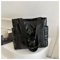 Detailed close-up of glossy black quilted down tote bag on minimalist white display stand - Black