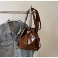 Detail of vintage brown glossy leather bucket bag featuring a silver butterfly charm and drawstring - Brown