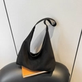Minimalist black hobo shoulder bag with wide strap displayed on an orange book - Black