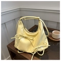 Close-up of cream yellow pleated cloud bag featuring bowknot details on wooden table - Yellow