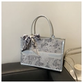 Detalle de bolso tote de jacquard gris plateado con pañuelo sobre sofá negro - Plateado