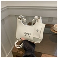 Close-up of white patent leather shoulder bag featuring a metal bow and knot handle - White