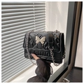 Detail of black quilted crossbody bag featuring silver butterfly buckle and chain strap - Black
