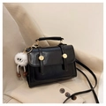 Detail of a black faux leather crossbody bag with gold hardware and a white plush charm - Black with Pendant