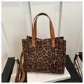 Dettaglio borsa tote leopardata con manici in pelle marrone su libro bianco e sedia - Leopardato Marrone Caramello (Marrone)