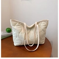 Gros plan sur la texture matelassée beige et la fine bandoulière de ce sac fourre-tout - Blanc