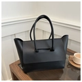 Detail of a black matte leather tote bag with unique flap-through handle on a glass table - Black