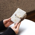 Handheld view of a short PU leather wallet with mushroom prints and a gold brand logo plate - Gray