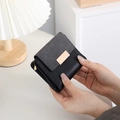 Close-up of black fold wallet showing textured leather finish and gold metal buckle - Black