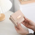 Detailed view of light pink compact wallet featuring a rose gold buckle and leather texture - Apricot