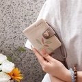 Close-up of cream PU leather wallet featuring leaf prints, bird charm, and a braided strap - Off White