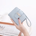 Close-up of light blue leather wallet with gold bow detail and wrist strap held by hand - Sky Blue