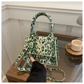 Dettaglio della borsa mini leopardata verde con logo S dorato e frange su tavolo in legno - Verde
