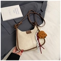 Detailansicht der cremefarbenen Schultertasche mit braunem Lederbesatz und Plüschanhänger - Mit Anhänger / Weiß
