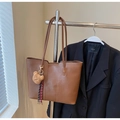 Close-up of a brown leather tote bag with a cute bear charm hanging on a metal rack - Brown with Pendant
