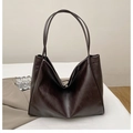 Detail of dark brown tote bag showing glossy leather texture and magnetic metal clasp - Brown