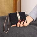 Detail of black knit texture wallet with golden leaf clasp and wrist strap being held - Black