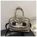 Detail of champagne gold quilted puffer bag featuring black handles and a shiny metallic finish - Gold