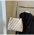 Detailansicht der beigen gesteppten Tragetasche mit goldener Kette neben schwarzem Blazer - Gebrochenes Weiß
