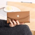 Dettaglio di un portafoglio lungo marrone in pelle PU con fibbia dorata tenuto in mano - Marrone