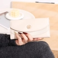 Dettaglio del portafoglio lungo in pelle beige con fibbia dorata e patta curva - Albicocca