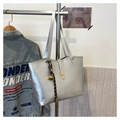Silver quilted tote bag with golden buckle and bell pendant on a minimalist metal rack - Silver