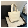 Close-up of a soft cream-colored tote bag placed on silk fabric near a black gift box - White