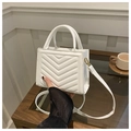 Detalle de un bolso bandolera acolchado blanco con patrón en V sobre mesa de madera - Blanco