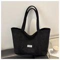 Detalle de bolso tote de pana negra con etiqueta blanca decorativa y bolsillo frontal exterior - Negro