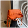 Close-up of orange crossbody bag with wave pattern flap and gold metal buckles - Orange