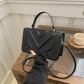 Elegant black leather crossbody bag with V-shaped quilting and gold hardware on a desk - Black