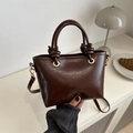Detailed view of brown leather handbag with gold hardware and embossed fashion text - Brown