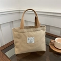 Mini sac à main en toile beige avec étiquette ours et anses tissées sur une table en bois - Kaki